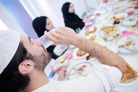 Eid Mubarak Muslim family having Iftar dinner drinking water to break feast. Eating traditional food...