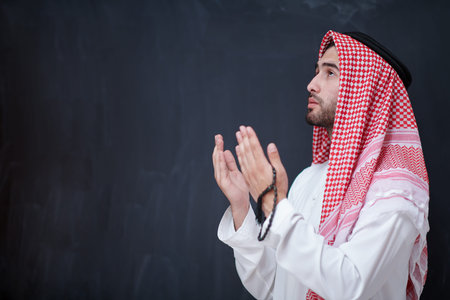 young arabian man in traditional clothes making traditional prayer to God, keeps hands in praying...
