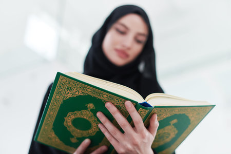 young traditional muslim woman reading Quran on the sofa before iftar dinner during a ramadan feast...