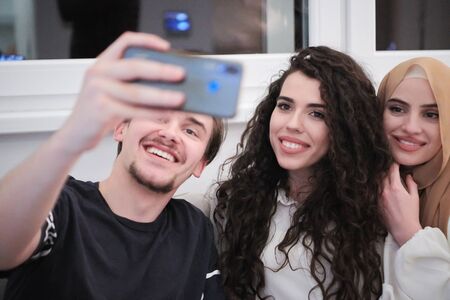 group of young muslim people one woman in fashionable dress with hijab using mobile phone while taking selfie picture at home representing modern islam fashion technology and ramadan kareem conceptの写真素材