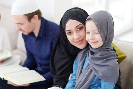 Traditional muslim family parents with children reading Quran and praying together on the sofa before iftar dinner during a ramadan feast at homeの写真素材