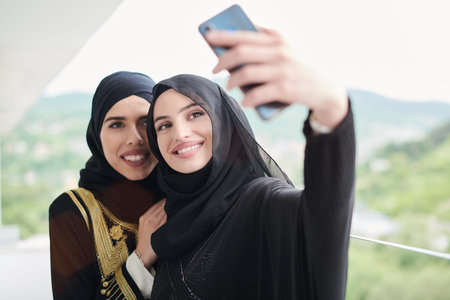 young beautiful muslim women in fashionable dress with hijab using mobile phone while taking selfie...