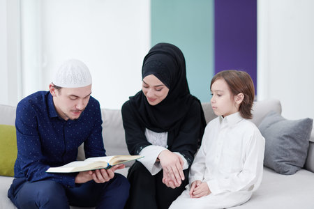 Traditional muslim family parents with children reading Quran and praying together on the sofa...
