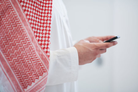 young modern muslim arabian businessman wearing traditional clothes while using smartphone at home
