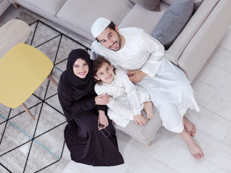 Traditional muslim family parents with children reading Quran and praying together on the sofa before iftar dinner during a ramadan feast at homeの写真素材