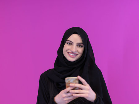 young modern muslim business woman using smartphone wearing hijab clothes isolated on pink...