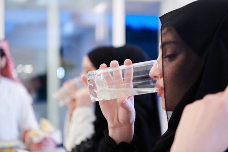 Eid Mubarak Muslim family having Iftar dinner drinking water to break feast. Eating traditional food during Ramadan feasting month at home. The Islamic Halal Eating and Drinking at modern western Islamの写真素材