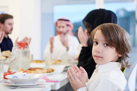 little muslim boy praying with traditional family before having iftar dinner together during a ramadan feast at homeの写真素材