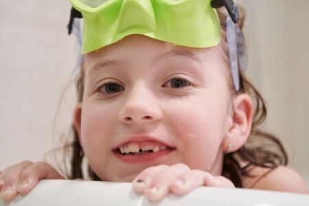 little girl with snorkel goggles in the tub while taking a bath in the bathtub, kids hygiene concept and summer vacation in corona virus stay at homeの写真素材