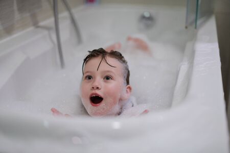 little girl playing with soap foam in bath during coronavirus stay at home pandemic quarantineの写真素材