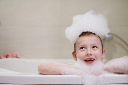 little girl playing with soap foam in bath during coronavirus stay at home pandemic quarantineの写真素材