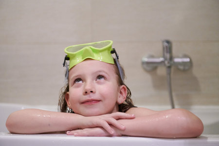 little girl with snorkel goggles in the tub while taking a bath in the bathtub, kids hygiene concept and summer vacation in corona virus stay at homeの写真素材
