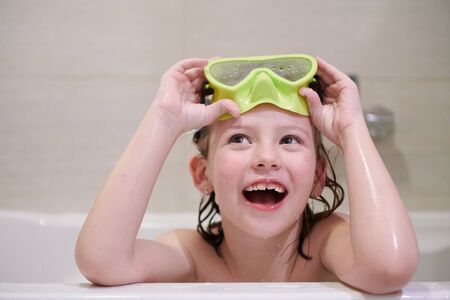 little girl with snorkel goggles in the tub while taking a bath in the bathtub, kids hygiene concept and summer vacation in corona virus stay at homeの写真素材