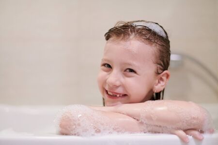 little girl playing with soap foam in bath during coronavirus stay at home pandemic quarantineの写真素材