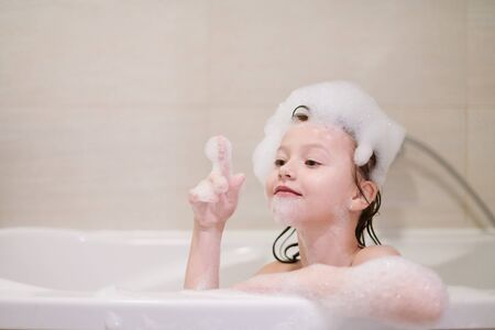 little girl playing with soap foam in bath during coronavirus stay at home pandemic quarantineの写真素材
