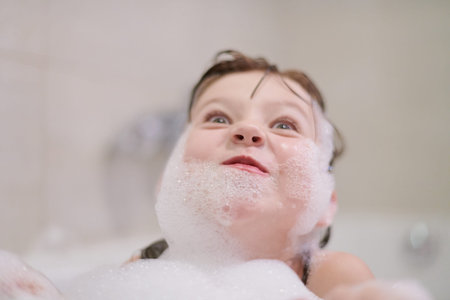 little girl playing with soap foam in bath during coronavirus stay at home pandemic quarantine