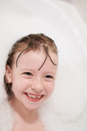 little girl playing with soap foam in bath during coronavirus stay at home pandemic quarantine
