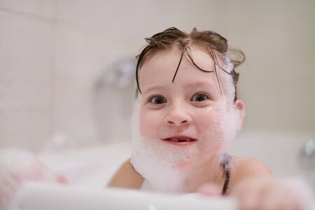 little girl playing with soap foam in bath during coronavirus stay at home pandemic quarantineの写真素材