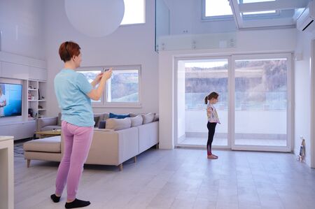 family at home little girl have online ballet training while mother is photographing her with smartphoneの写真素材