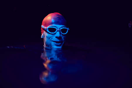 authentic triathlete swimmer having a break during hard training on night neon gel lightの写真素材