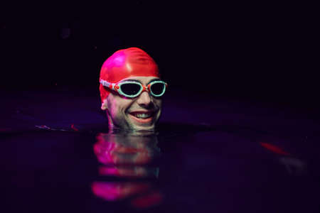 authentic triathlete swimmer having a break during hard training on night neon gel lightの写真素材