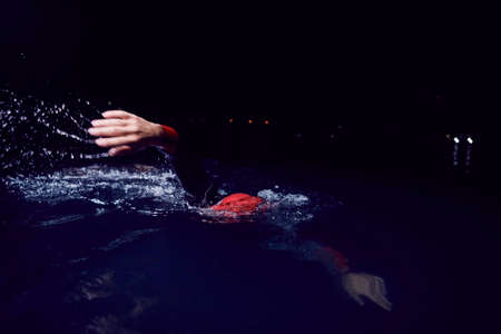 triathlon athlete swimming in dark night wearing wetsuitの写真素材