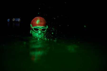 authentic triathlete swimmer having a break during hard training on night neon gel lightの写真素材
