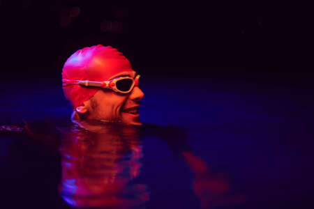 authentic triathlete swimmer having a break during hard training on night neon gel lightの写真素材