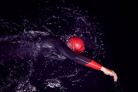 triathlon athlete swimming in dark night wearing wetsuit
