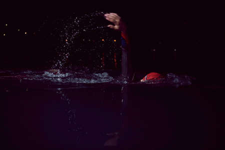 triathlon athlete swimming in dark night wearing wetsuitの写真素材