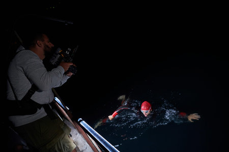 videographer taking action shot of triathlon swimming athlete at night