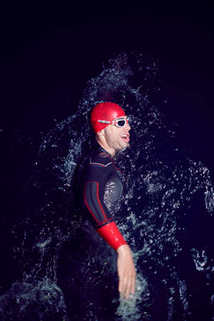 triathlon athlete swimming in dark night wearing wetsuitの写真素材