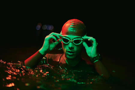 authentic triathlete swimmer having a break during hard training on night neon gel lightの写真素材