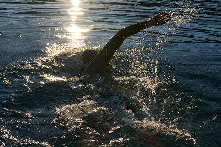 triathlon athlete swimming on lake in sunrise wearing wetsuitの写真素材