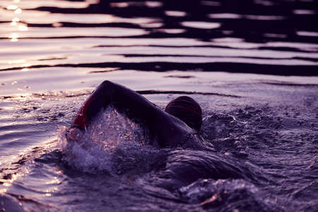 triathlon athlete swimming on lake in sunrise wearing wetsuitの写真素材