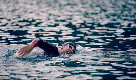 triathlon athlete swimming on lake in sunrise wearing wetsuitの写真素材