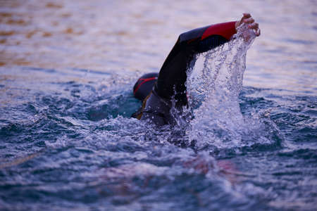 triathlon athlete swimming on lake in sunrise wearing wetsuit