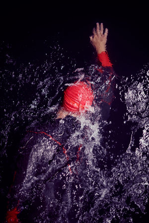 triathlon athlete swimming in dark night wearing wetsuit