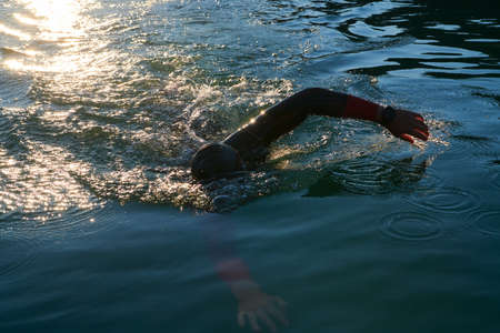 triathlon athlete swimming on lake in sunrise wearing wetsuitの写真素材