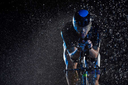 triathlon athlete riding bike fast on rainy nightの写真素材