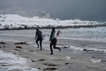 Arctic surfers running on beach after surfingの写真素材
