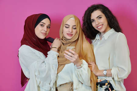 Muslim women using mobile phones isolated on pink backgroundの写真素材