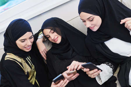 Portrait of Arabian girls wearing modern abaya using mobile phoneの写真素材