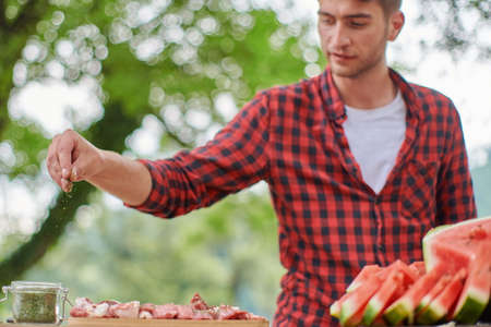 man putting spices on raw meat for barbecueの写真素材
