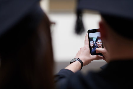 group of happy international students in mortar boards and bachelor gowns with diplomas taking...