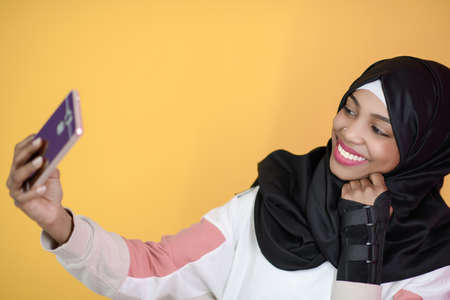 african muslim woman with a beautiful smile takes a selfie with a cell phoneの写真素材