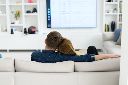 young couple watching tv at home in bright living room