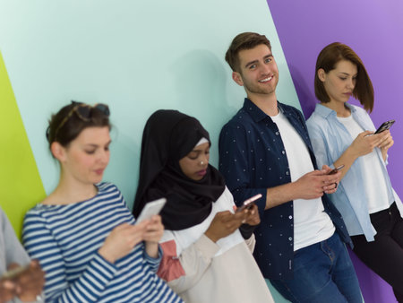 diverse teenagers use mobile devices while posing for a studio photo in front of a pink background