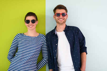 Beautiful young loving couple adjusting their sunglasses while standing against green-grey...