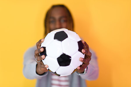 afro man posing on a yellow background while holding a soccer ball